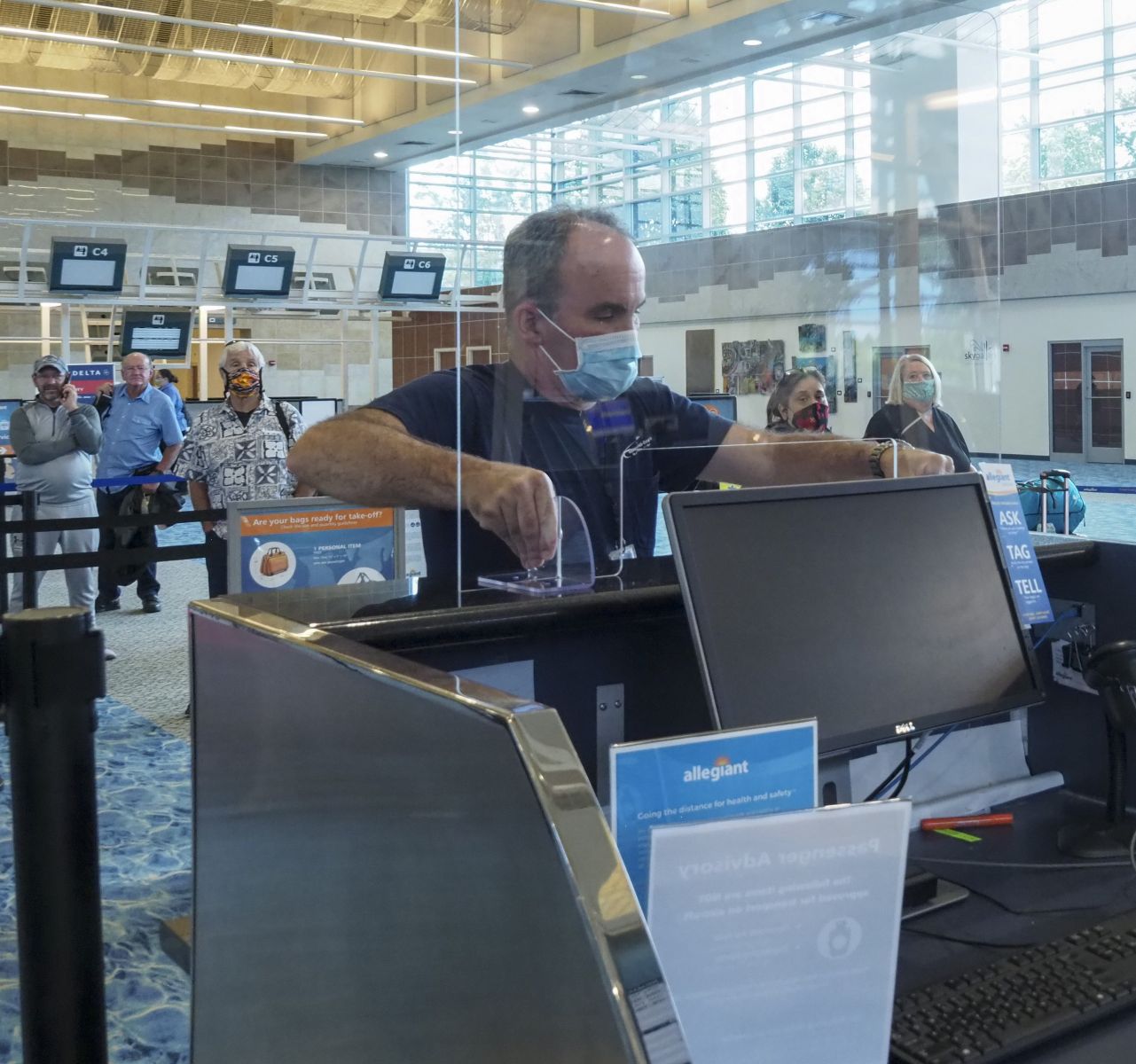 Airport staff installs sneeze guard at ticket counter.